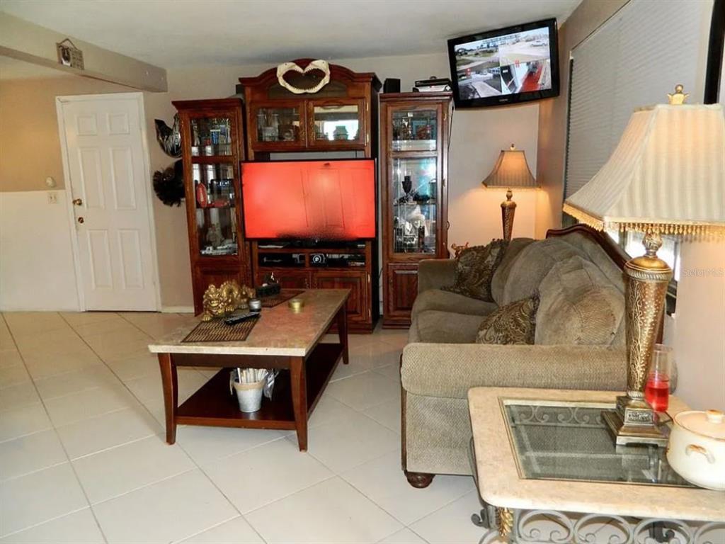A living room features tile flooring, a large wooden entertainment center, and a beige sofa — 3442 WILTSHIRE DRIVE, HOLIDAY, FL