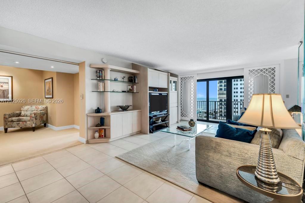 A living room features light tile floors, a built-in shelving unit, and a balcony view — 1201 S Ocean Dr # 2003N, Hollywood FL 33019, HOLLYWOOD, FL