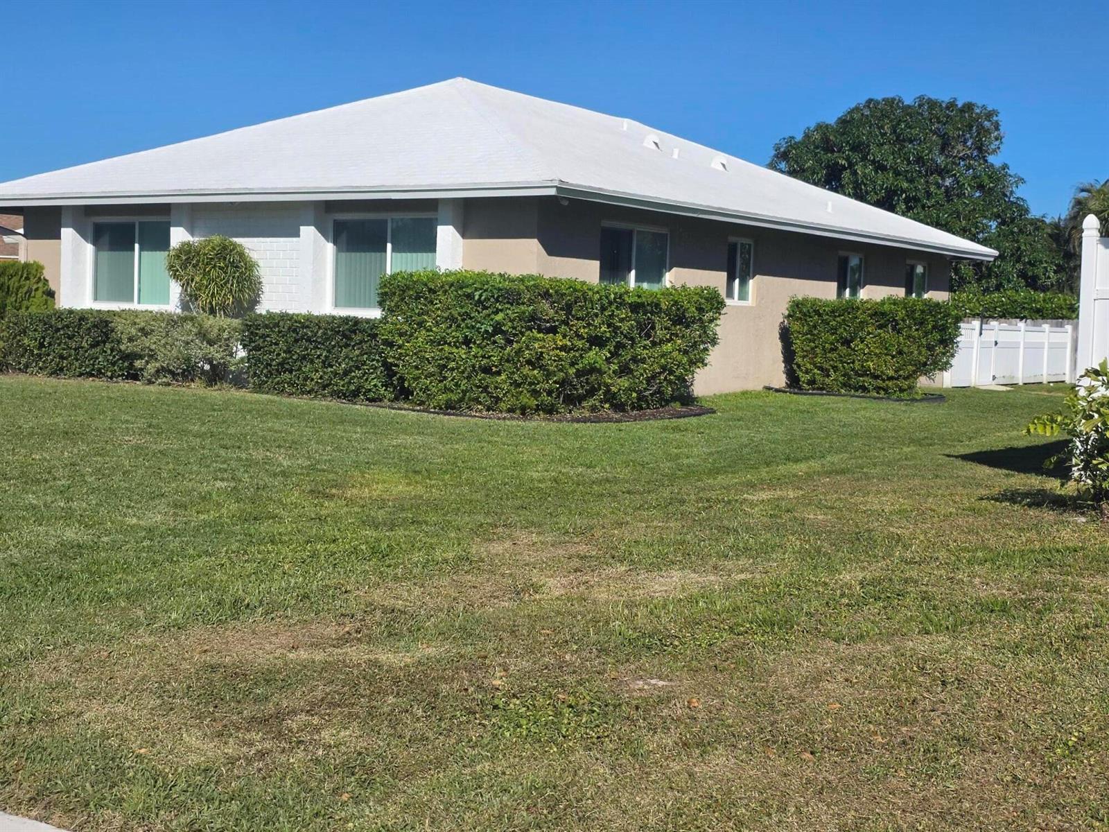 A single-story house with a white roof, tan exterior, and manicured hedges in the front yard — 27 Vista Del Rio, Boynton Beach FL 33426, BOYNTON BEACH, FL