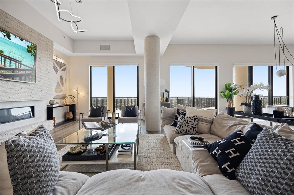 A modern living room features a fireplace, large windows, a central pillar, and neutral furniture — 14300 RIVA DEL LAGO DRIVE UNIT 2104, FORT MYERS, FL