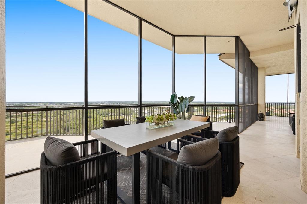 A covered balcony features a dining set, tiled flooring, and expansive views through screened walls — 14300 RIVA DEL LAGO DRIVE UNIT 2104, FORT MYERS, FL