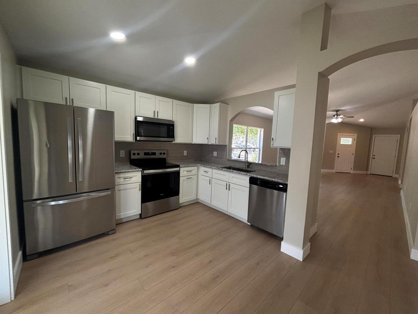 A kitchen with white cabinets, stainless steel appliances, and light wood flooring — 1001 Harvest Moon Drive, FL 33584, FL