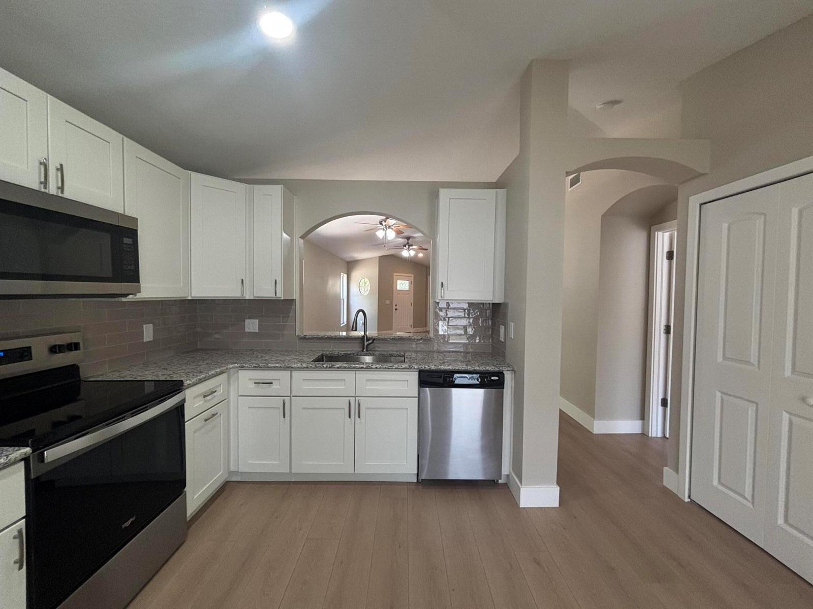 A kitchen features white cabinets, granite countertops, stainless steel appliances, and a pass-through arched window — 1001 Harvest Moon Drive, FL 33584, FL