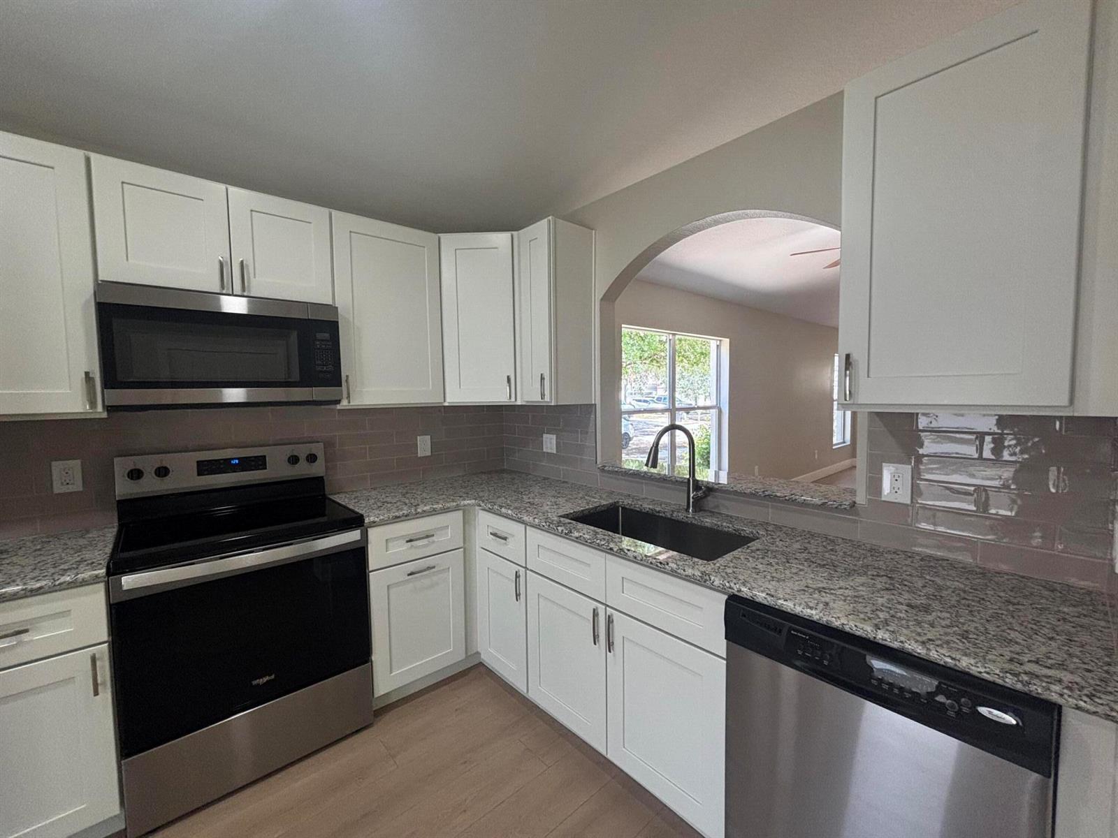 A kitchen features white cabinets, granite countertops, stainless steel appliances, and a pass-through arched window — 1001 Harvest Moon Drive, FL 33584, FL