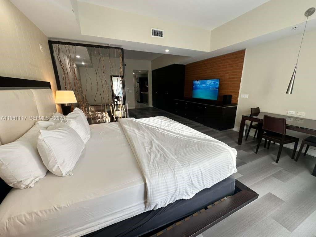 A studio apartment features a living area with a sofa, a bed, and wood-look flooring — 5300 NW 87th Ave # 910, Doral FL 33178, DORAL, FL