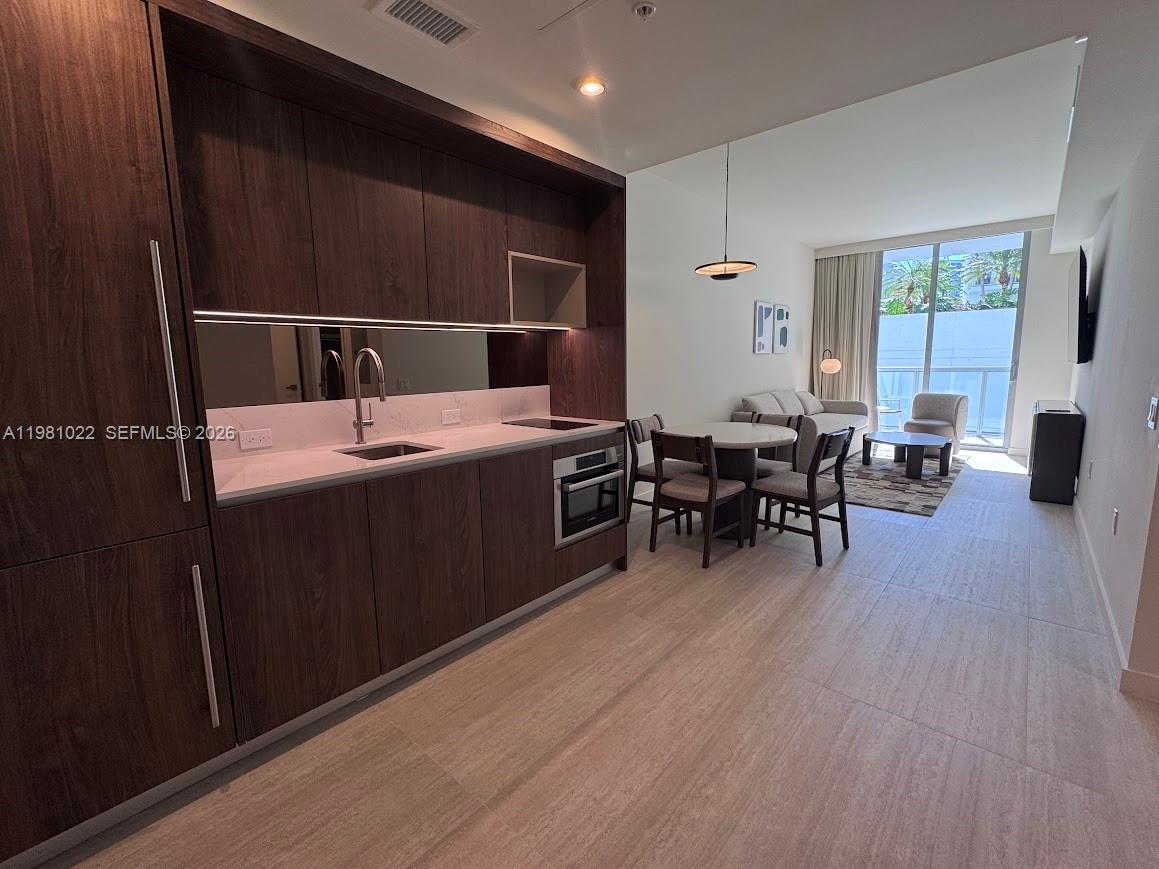 A modern kitchen with dark wood cabinetry and white countertops opens into a living area — 1611 SW 2nd Av # 306, Miami FL 33129, MIAMI, FL