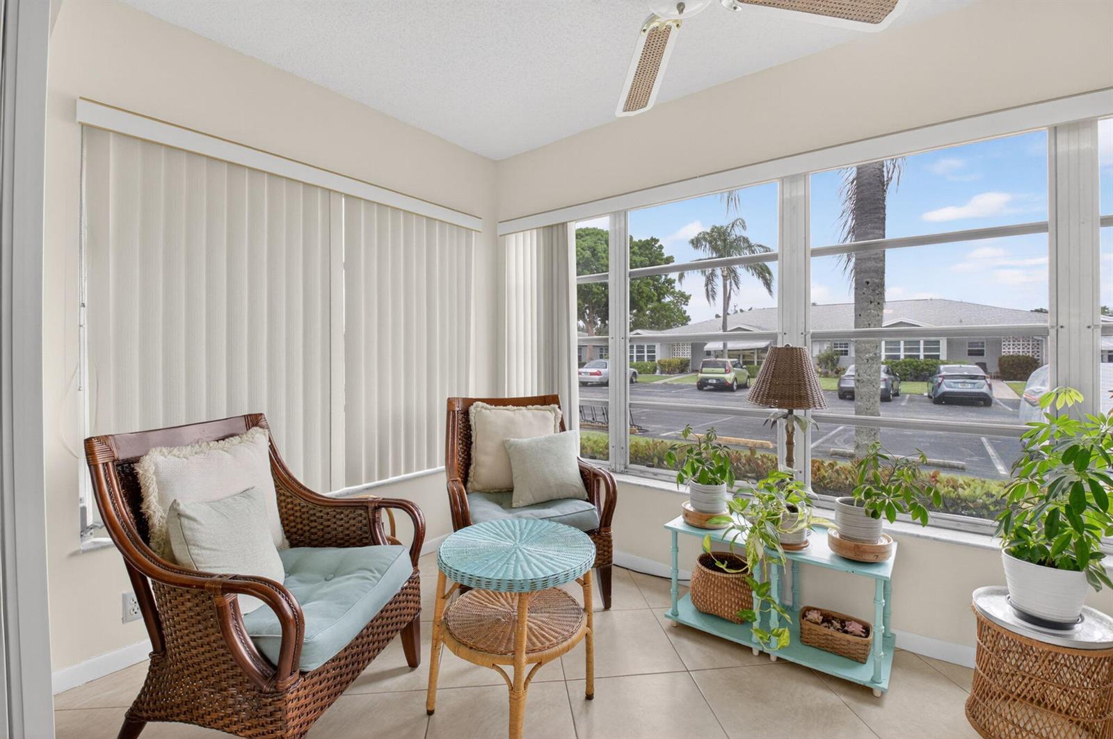 A sunroom features wicker furniture, a light blue side table, potted plants, and large windows — 14579 Canalview Drive # B, Delray Beach FL 33484, DELRAY BEACH, FL