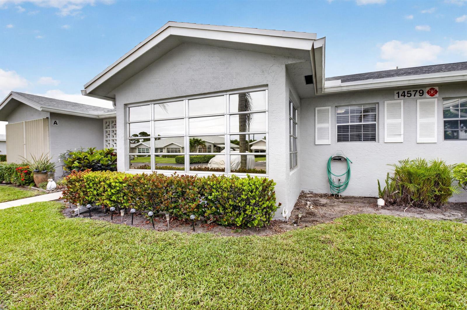 A single-story gray house with a large window, a green garden hose, and landscaping — 14579 Canalview Drive # B, Delray Beach FL 33484, DELRAY BEACH, FL