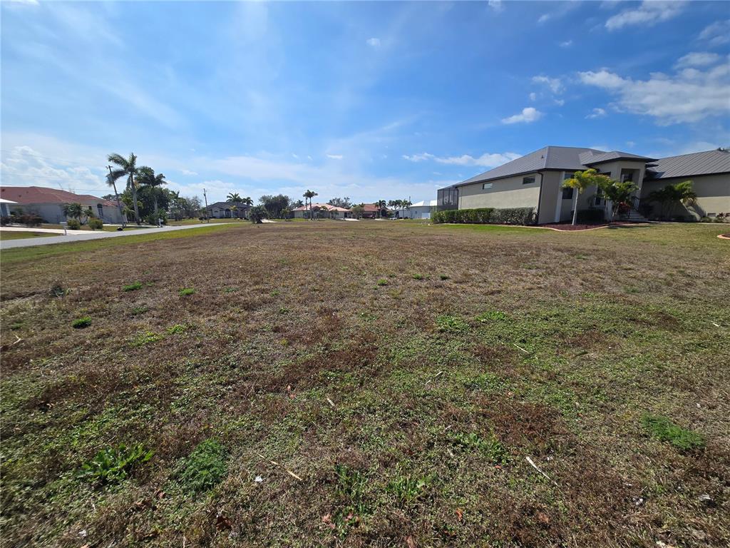 A vacant, grassy residential lot sits in a suburban neighborhood with nearby houses — 24355 MATIAS LANE, PUNTA GORDA, FL