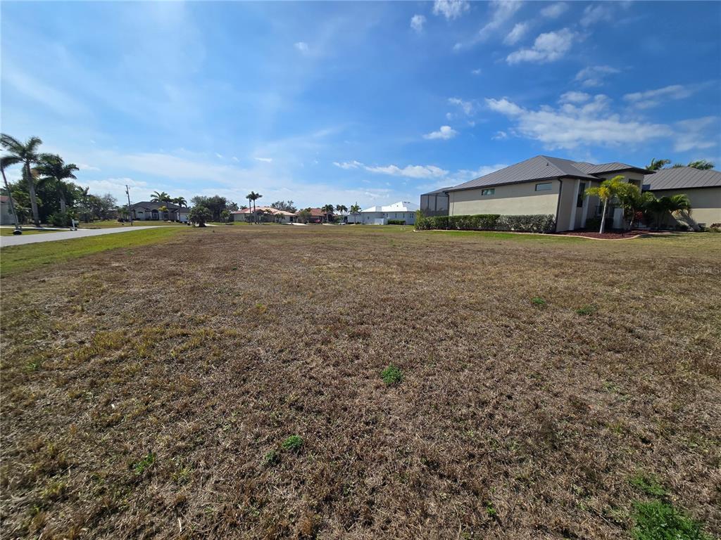 A large, vacant residential lot with dry grass and surrounding houses under a blue sky — 24355 MATIAS LANE, PUNTA GORDA, FL