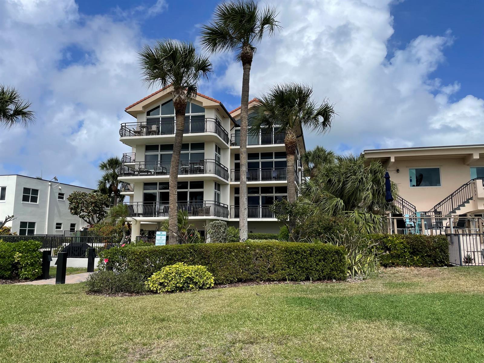 A three-story building with balconies and palm trees stands behind a manicured hedge — 314 Inlet Way # 201, Palm Beach Shores FL 33404, PALM BEACH SHORES, FL
