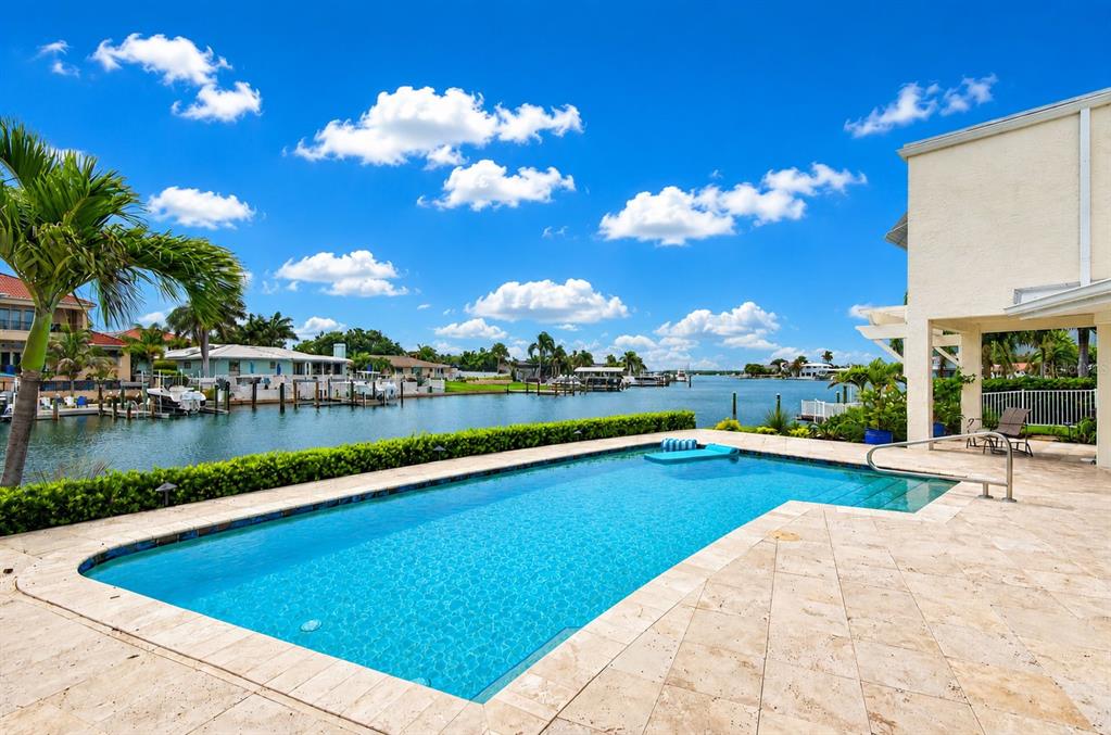 A rectangular swimming pool sits on a stone patio overlooking a canal with boat docks — 812 SNUG ISLAND, CLEARWATER BEACH, FL