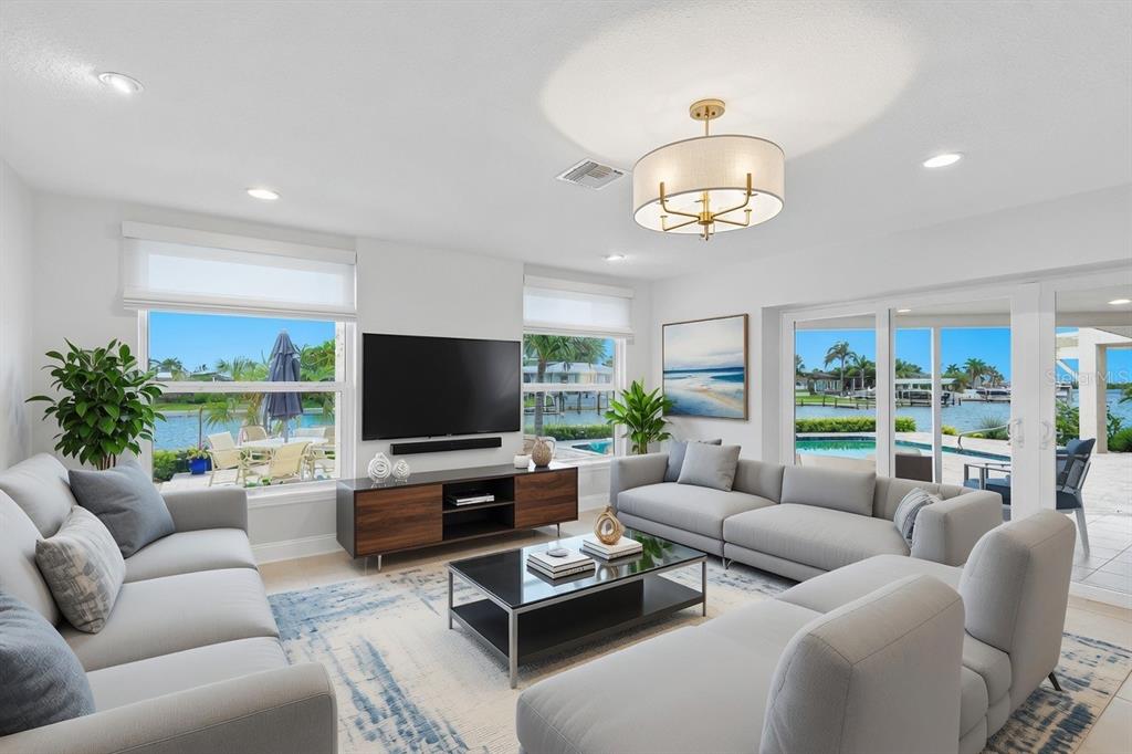 A living room with gray sofas, a glass coffee table, and views of a waterfront pool — 812 SNUG ISLAND, CLEARWATER BEACH, FL