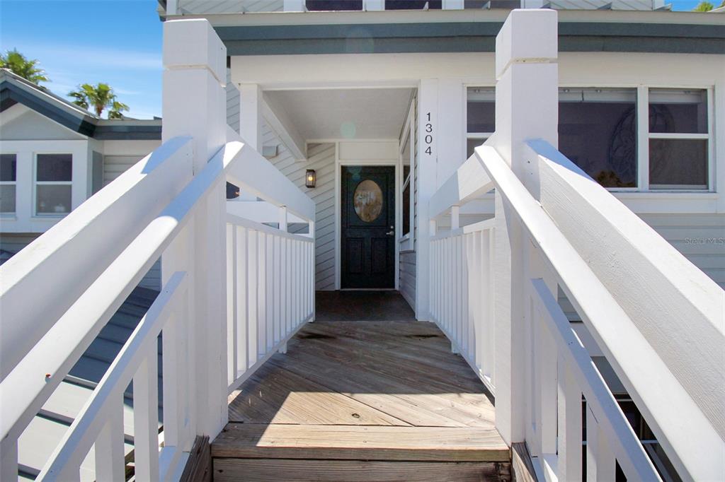 A wooden walkway with white railings leads to a dark front door of a house — 1304 SIESTA BAYSIDE DRIVE UNIT 1304B, SARASOTA, FL