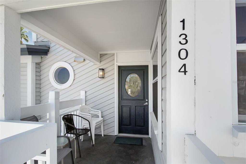 A covered front porch features a black door, white siding, and a small seating area — 1304 SIESTA BAYSIDE DRIVE UNIT 1304B, SARASOTA, FL