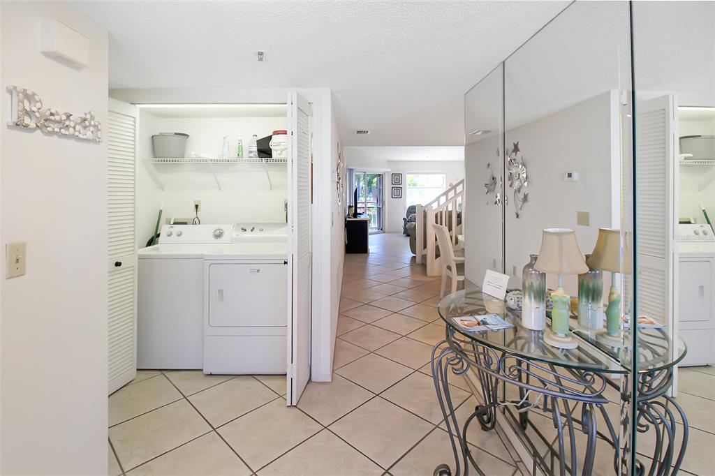 A hallway with a laundry closet, tiled floors, and a glass-topped console table with lamps — 1304 SIESTA BAYSIDE DRIVE UNIT 1304B, SARASOTA, FL