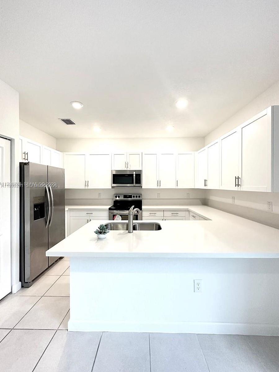 A modern kitchen features white cabinets, stainless steel appliances, and a white quartz countertop island — 20800 NE 5th Ct, Miami FL 33179, MIAMI, FL