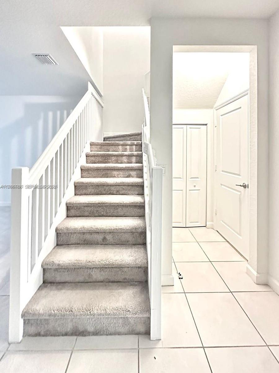 A carpeted staircase with a white railing leads upward next to a tiled hallway — 20800 NE 5th Ct, Miami FL 33179, MIAMI, FL