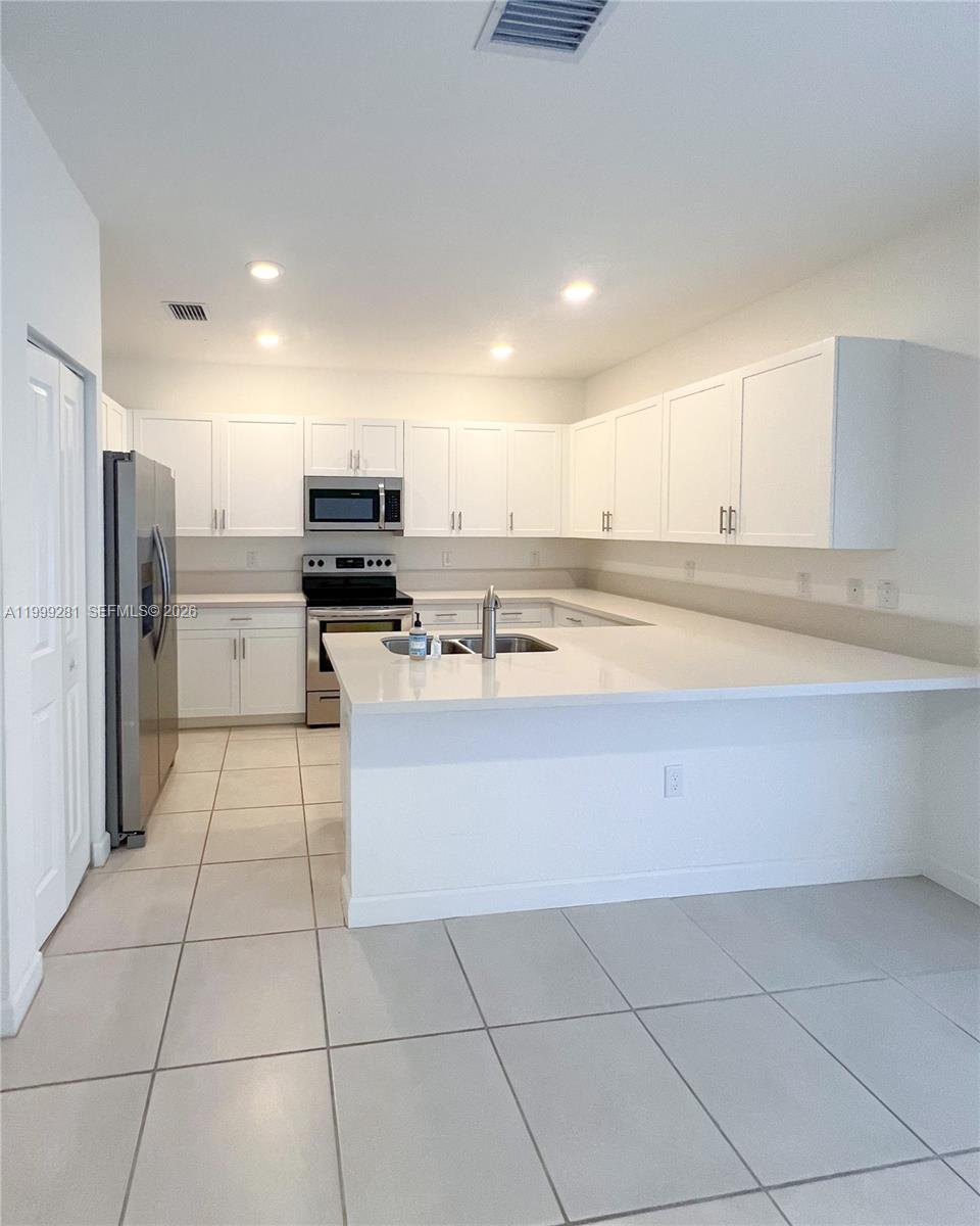 A kitchen features white cabinets, stainless steel appliances, and a peninsula with a sink — 20800 NE 5th Ct, Miami FL 33179, MIAMI, FL