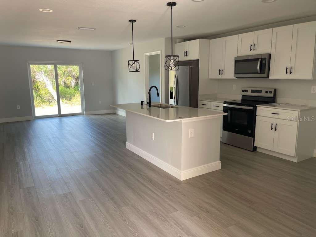 A modern kitchen features white cabinets, stainless steel appliances, and a central island with lighting — 17512 POSTON AVENUE, PORT CHARLOTTE, FL