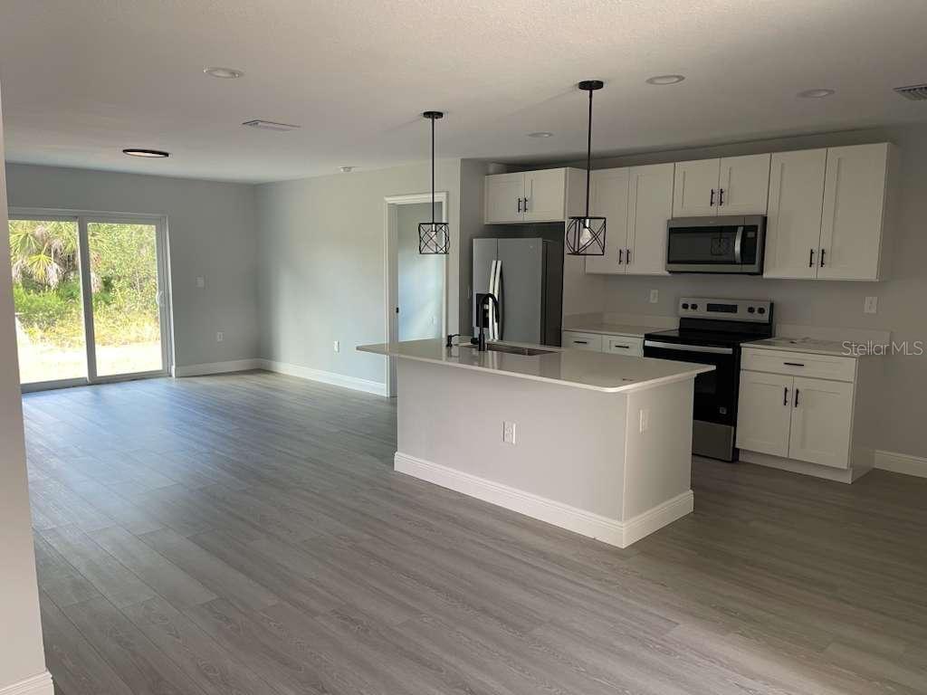 A kitchen with white cabinets and a center island opens to a living area — 17512 POSTON AVENUE, PORT CHARLOTTE, FL