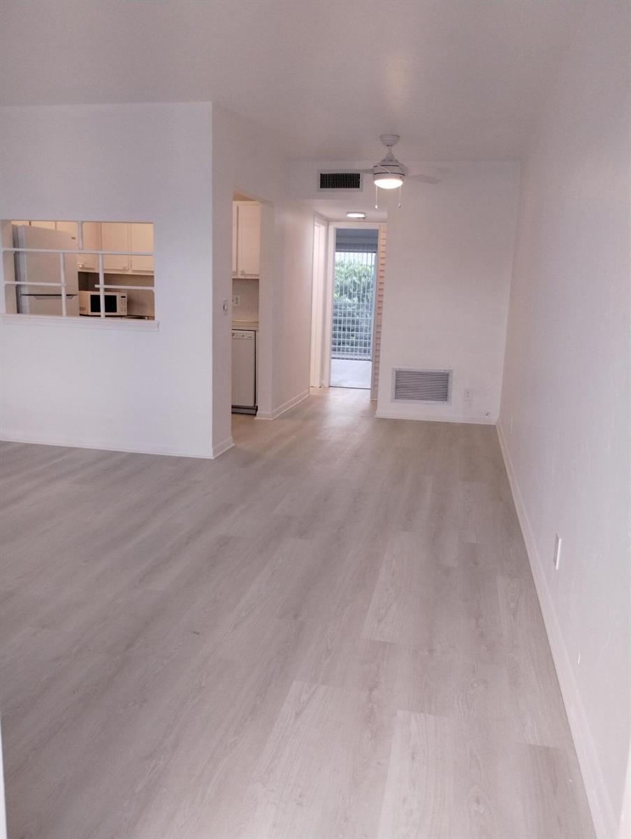 An empty room with light wood-look flooring, a ceiling fan, and a kitchen pass-through window — 2880 Lake Osborne Drive # 209, FL 33461, FL
