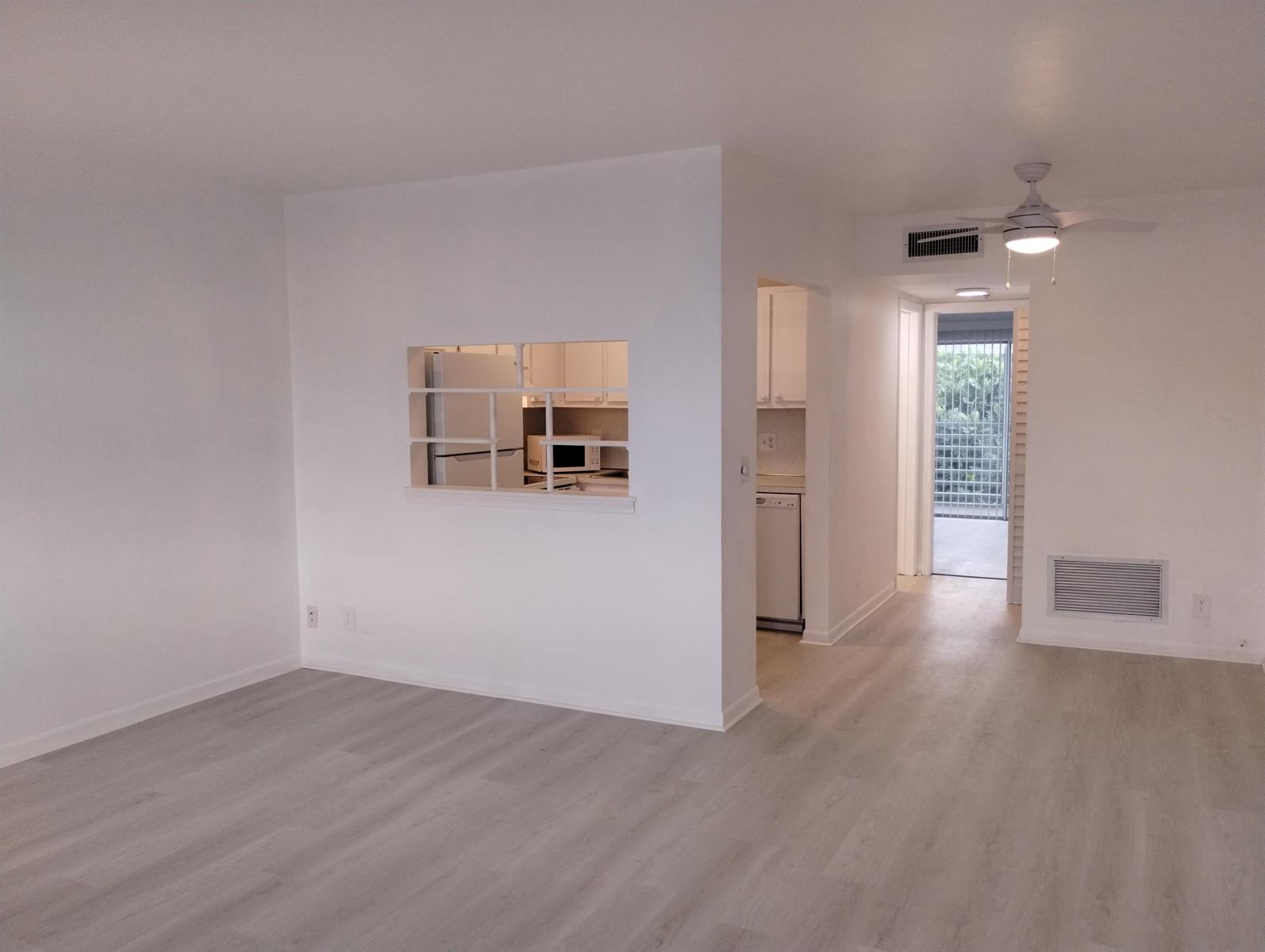 An empty living room with light wood-look flooring, a ceiling fan, and a kitchen pass-through — 2880 Lake Osborne Drive # 209, FL 33461, FL