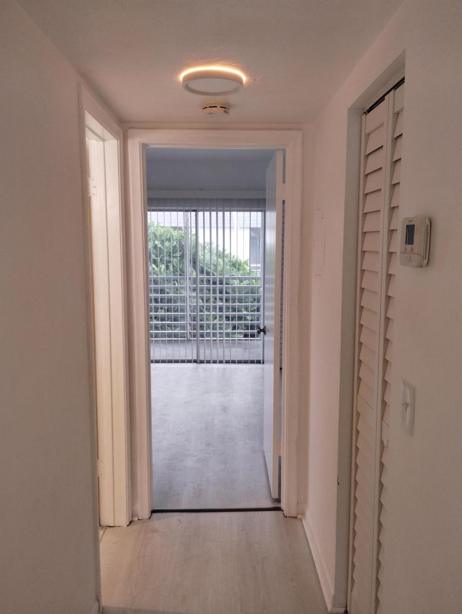 A hallway with light wood-look flooring leads to a room with a sliding glass door — 2880 Lake Osborne Drive # 209, FL 33461, FL