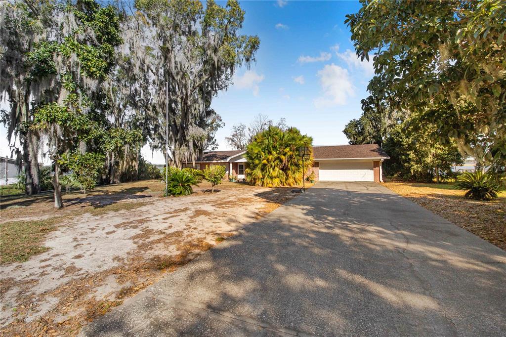 A single-story house with a concrete driveway, a two-car garage, and large moss-draped trees — 436 JEFFERY LANE, HAINES CITY, FL