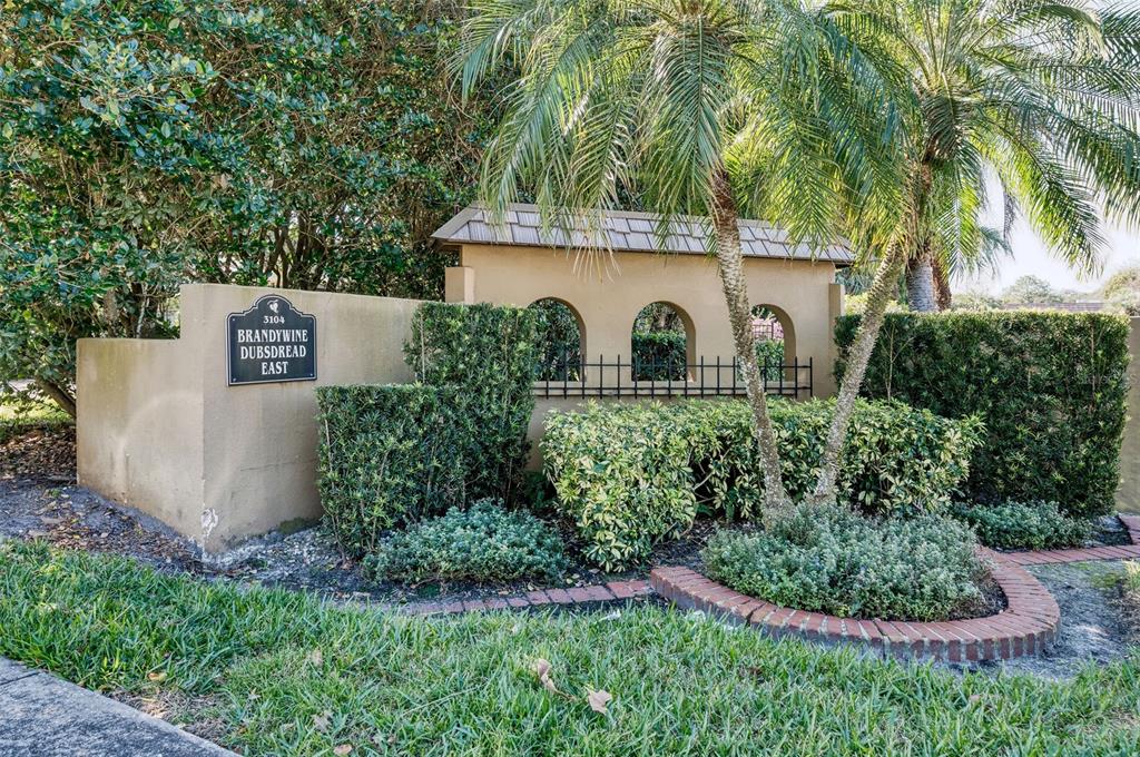 A tan stucco wall with arched cutouts and a sign marks the entrance to a community — 3104 HARRISON AVENUE UNIT C 18, ORLANDO, FL