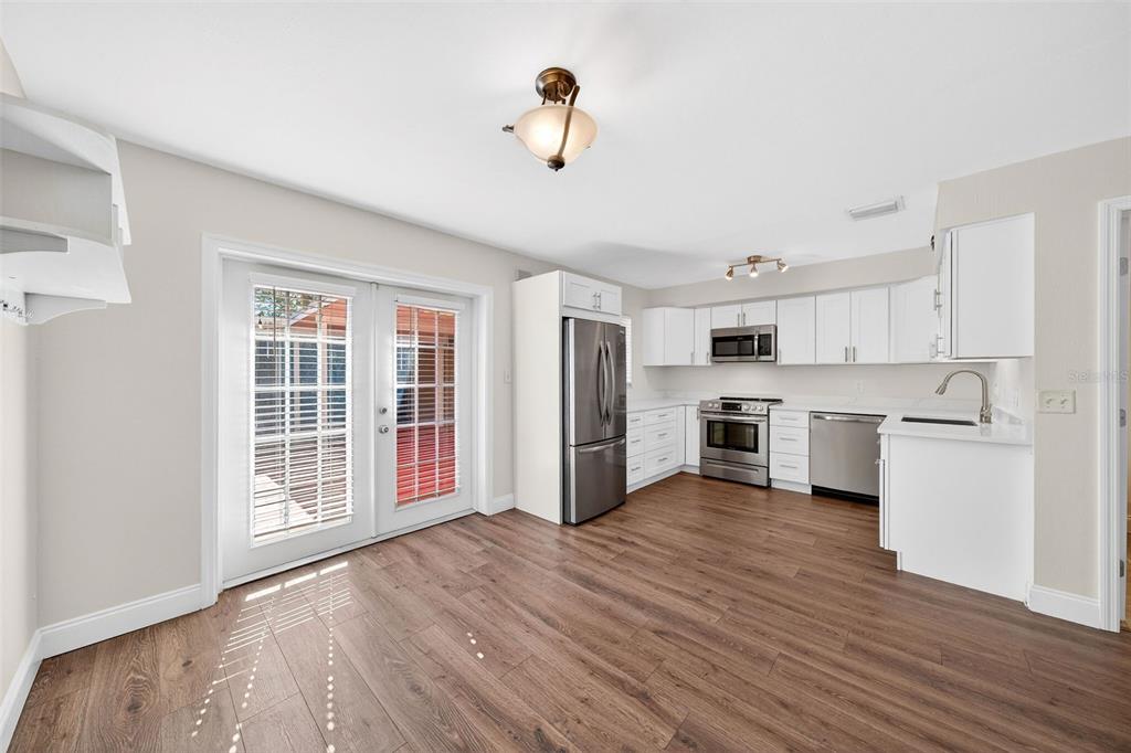 A kitchen with white cabinets, stainless steel appliances, and wood-look flooring leads to a patio — 3104 HARRISON AVENUE UNIT C 18, ORLANDO, FL