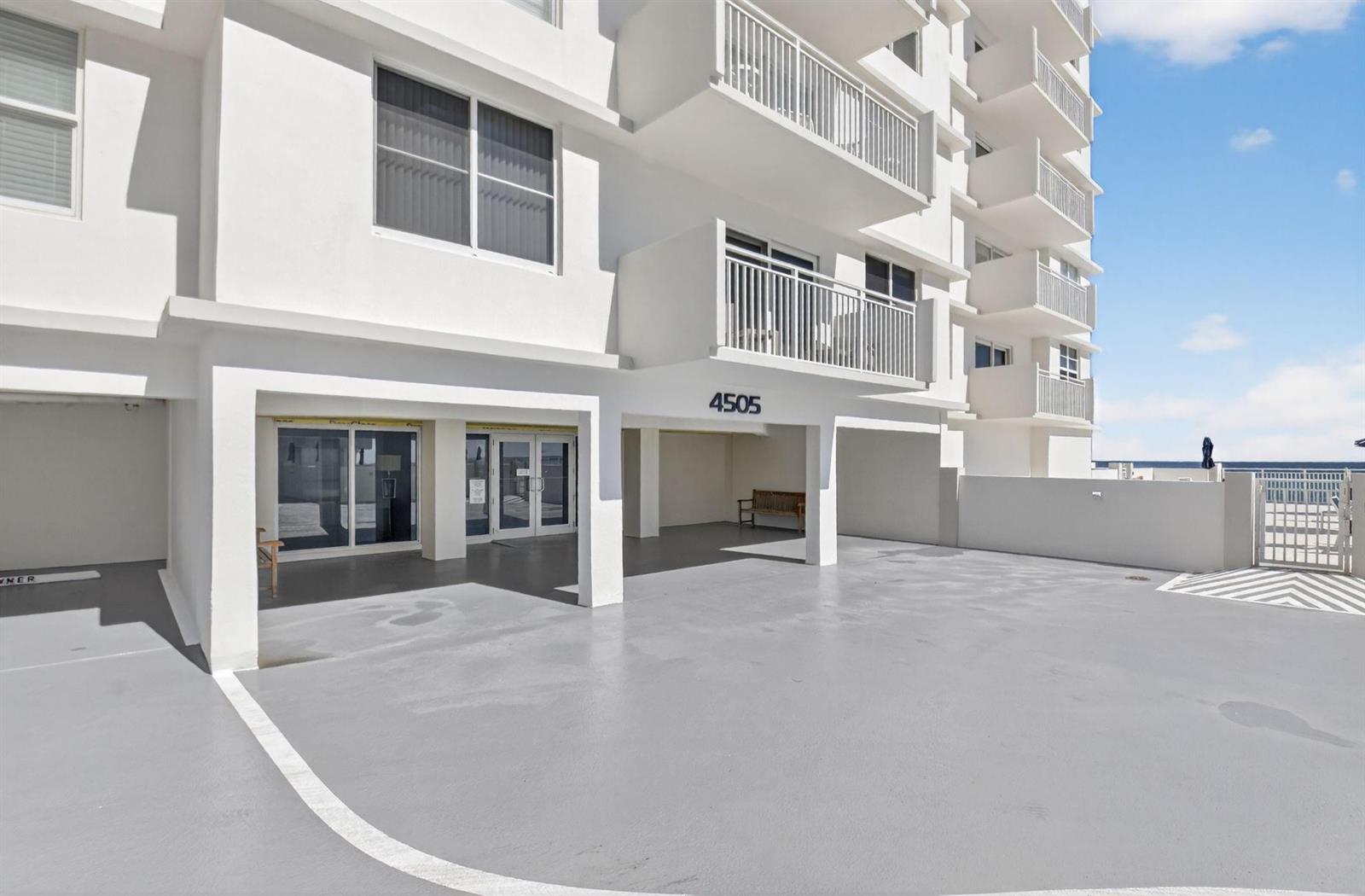 The exterior of a white multi-story building features a covered parking area and balconies — 4505 S Ocean Boulevard # 805, Highland Beach FL 33487, HIGHLAND BEACH, FL