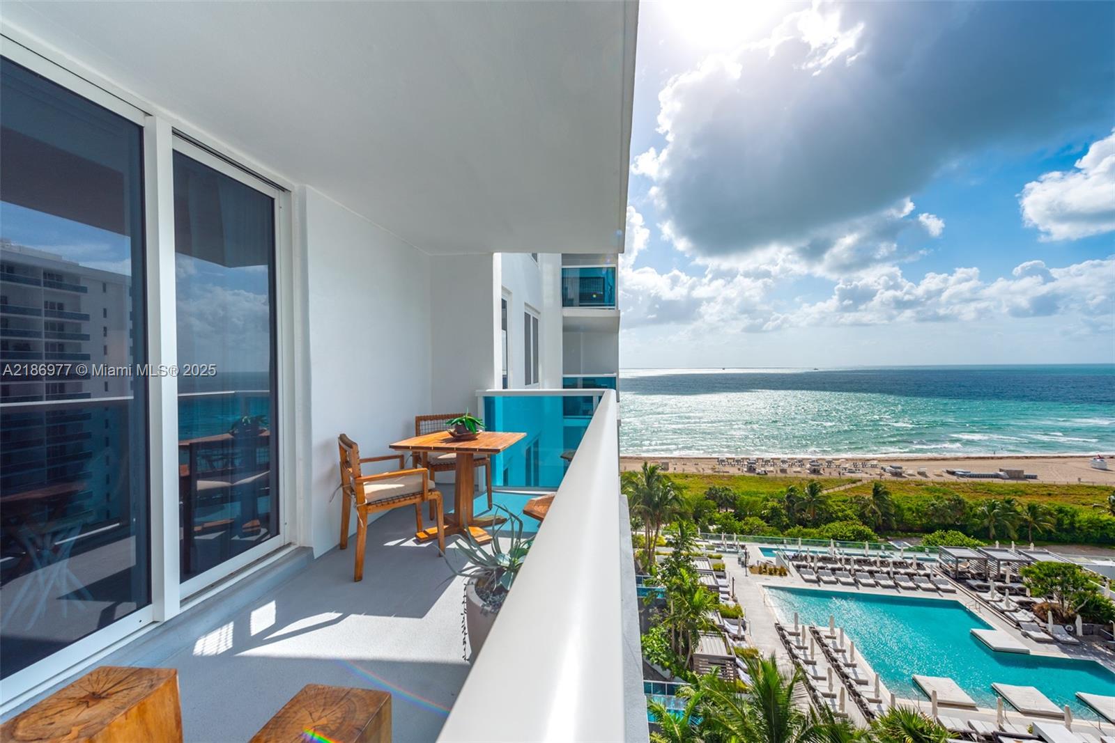 A balcony with a small wooden table and chairs overlooks a swimming pool and ocean — 102 24 ST # 1408, Miami Beach FL 33139, MIAMI BEACH, FL