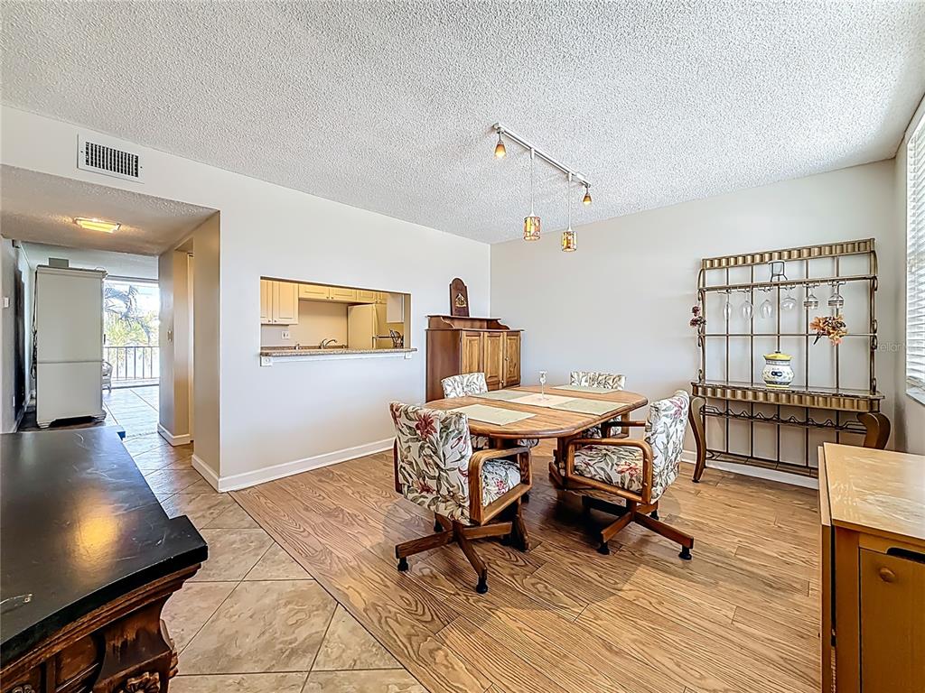 A dining room with wood-look flooring, a wooden table, floral chairs, and a metal hutch — 7401 BAY ISLAND DRIVE S UNIT 232, SOUTH PASADENA, FL