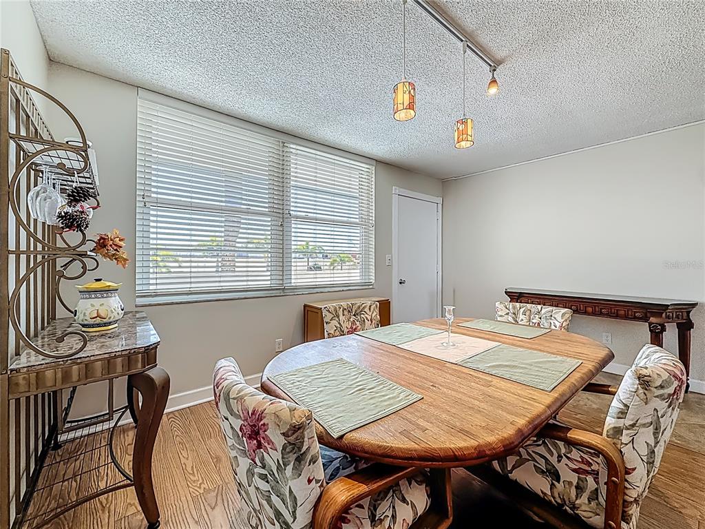 A dining room features a wooden table, floral chairs, a metal baker's rack, and blinds — 7401 BAY ISLAND DRIVE S UNIT 232, SOUTH PASADENA, FL