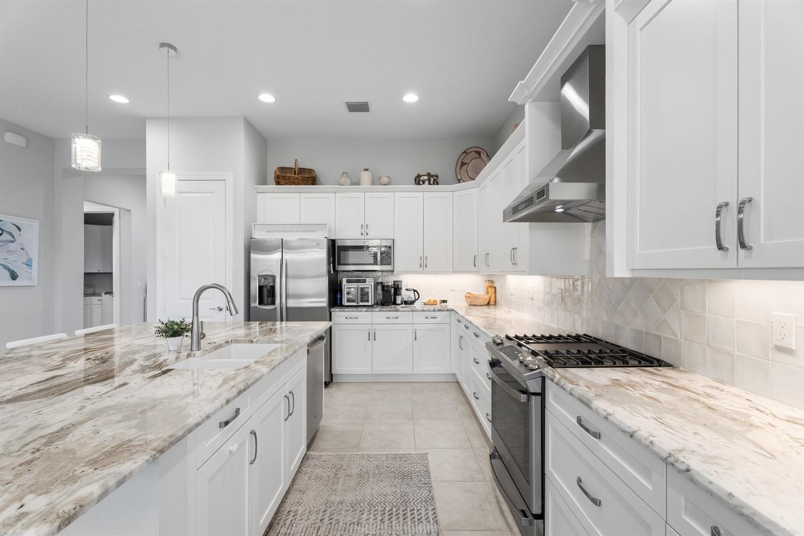 A modern kitchen features white cabinetry, marble countertops, stainless steel appliances, and a central island — 6390 High Pointe West Way, Vero Beach FL 32967, VERO BEACH, FL