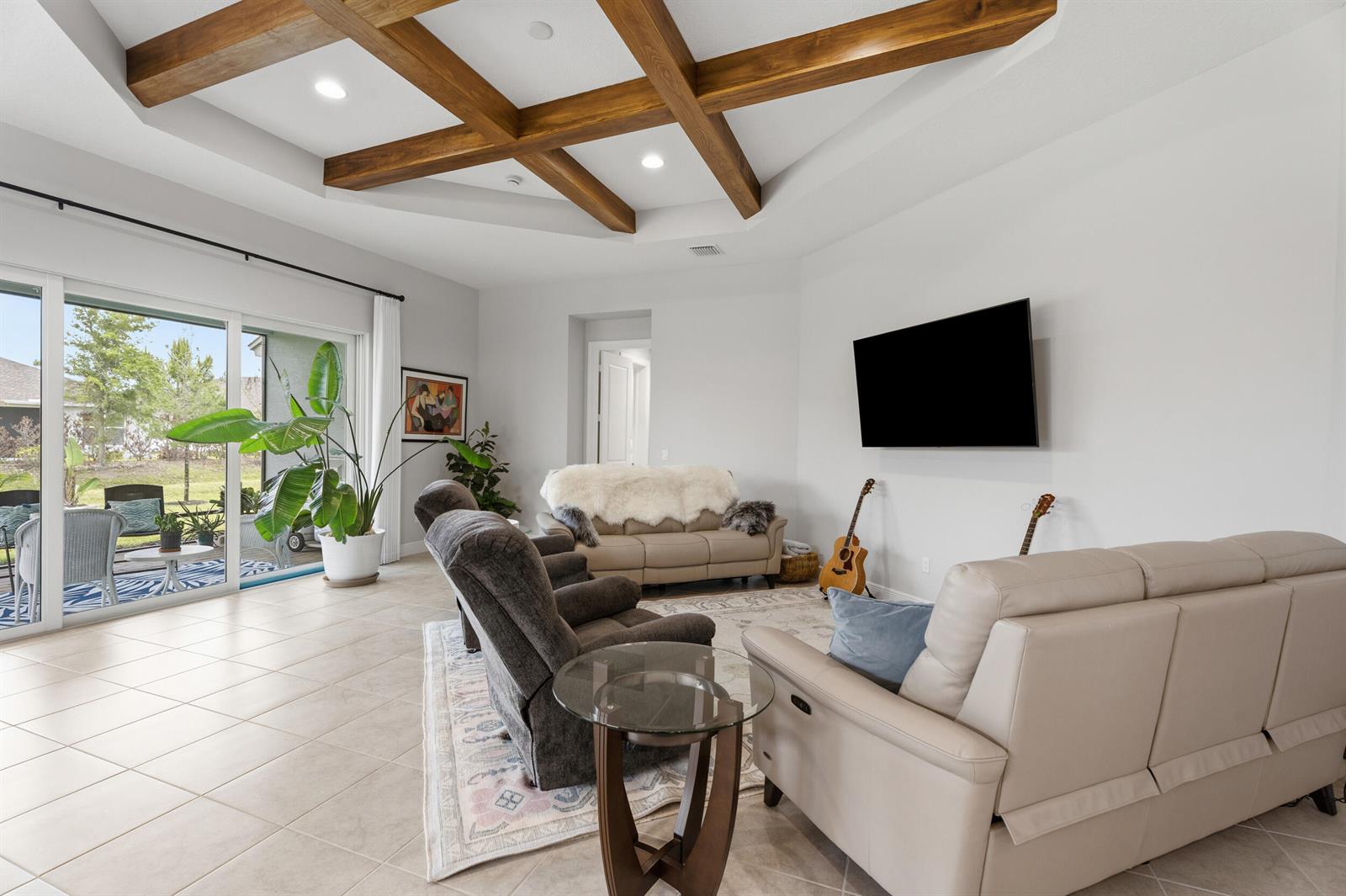 A living room features a coffered ceiling with wood beams, tile floors, and sliding doors — 6390 High Pointe West Way, Vero Beach FL 32967, VERO BEACH, FL