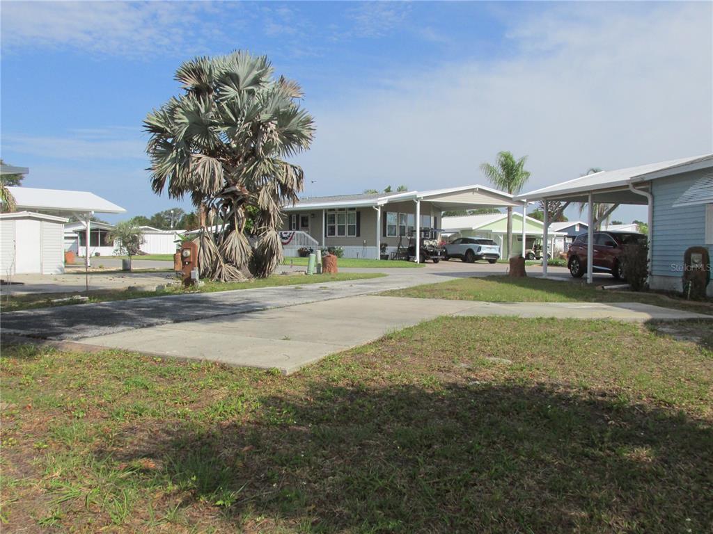 A view of a mobile home with a carport, driveway, and a large palm tree — 15 RED QUILL CIRCLE, LAKE WALES, FL