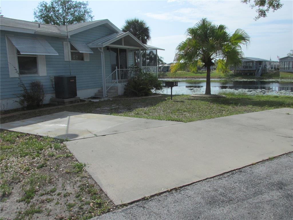 A light blue mobile home with a concrete driveway sits beside a small pond — 15 RED QUILL CIRCLE, LAKE WALES, FL