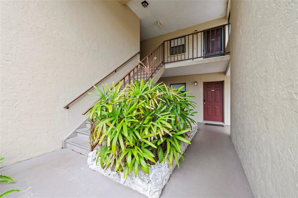 An outdoor staircase leads to an upper-level balcony beside a ground-floor entrance with landscaping — 7217 CLOISTER DRIVE UNIT 203, SARASOTA, FL