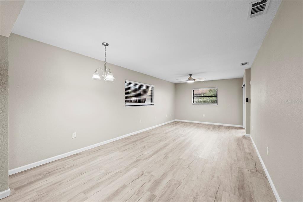 An empty room features light wood-look flooring, beige walls, a ceiling fan, and a chandelier — 7217 CLOISTER DRIVE UNIT 203, SARASOTA, FL