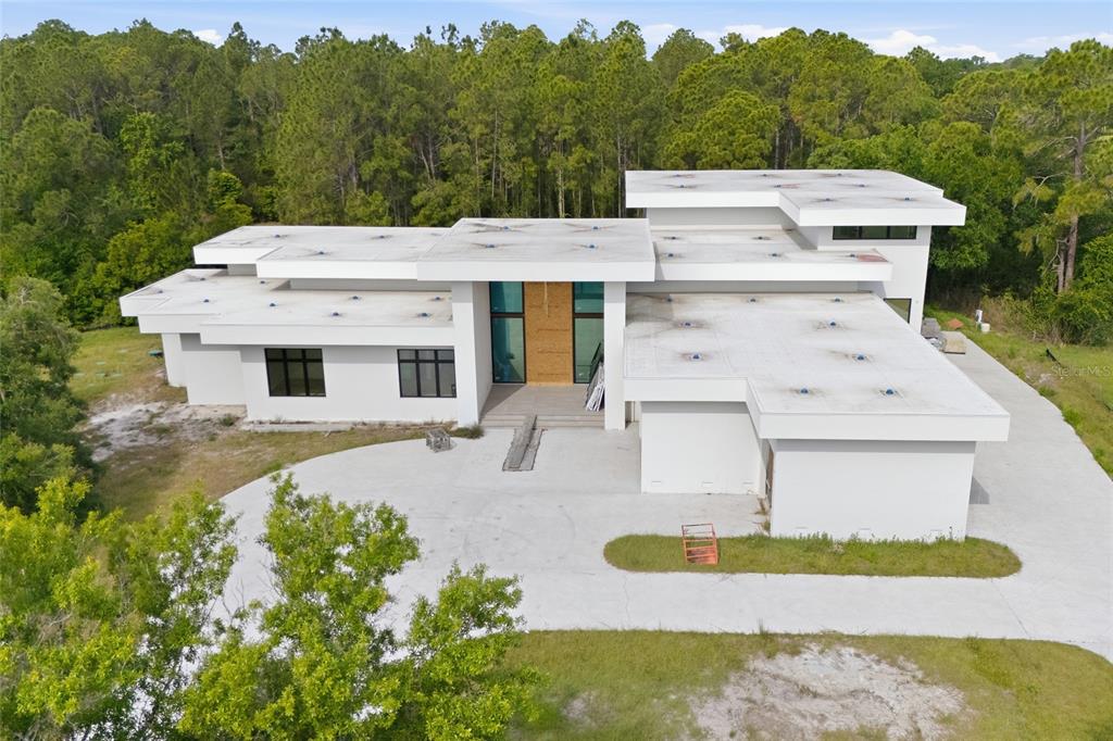 An aerial view of a modern, flat-roofed white house under construction surrounded by trees — 12505 STONELAKE RANCH BOULEVARD, THONOTOSASSA, FL