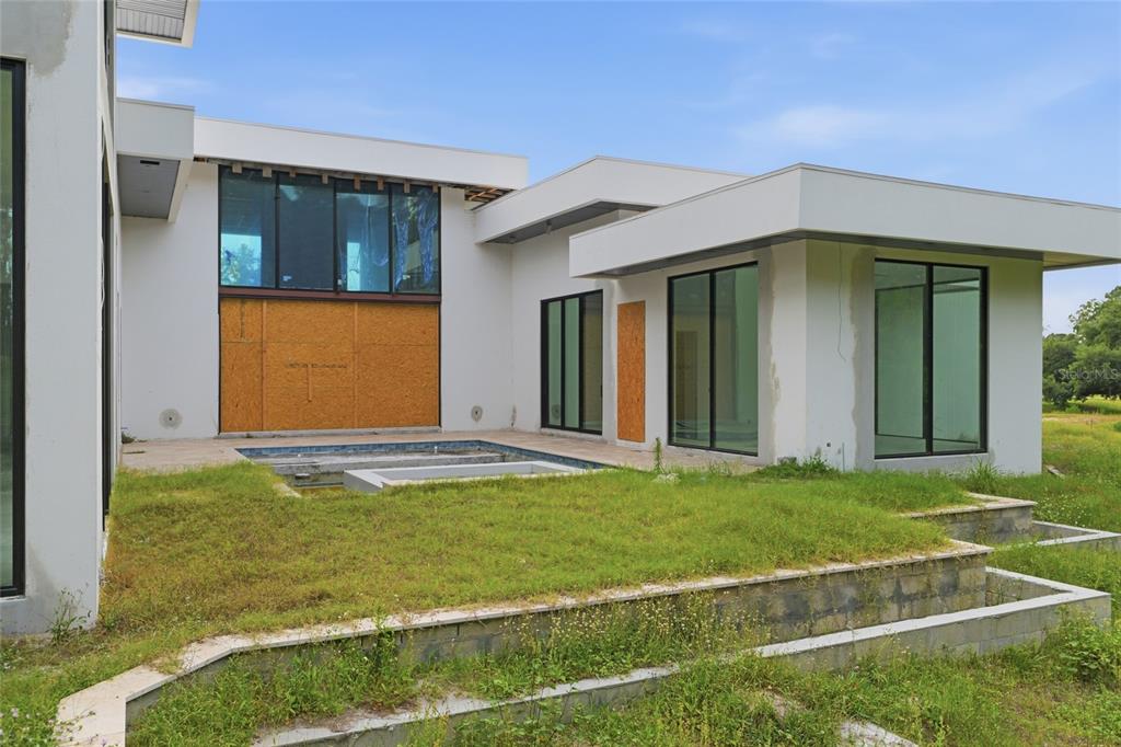 An unfinished modern house exterior features a pool, patio, and plywood-covered window openings — 12505 STONELAKE RANCH BOULEVARD, THONOTOSASSA, FL