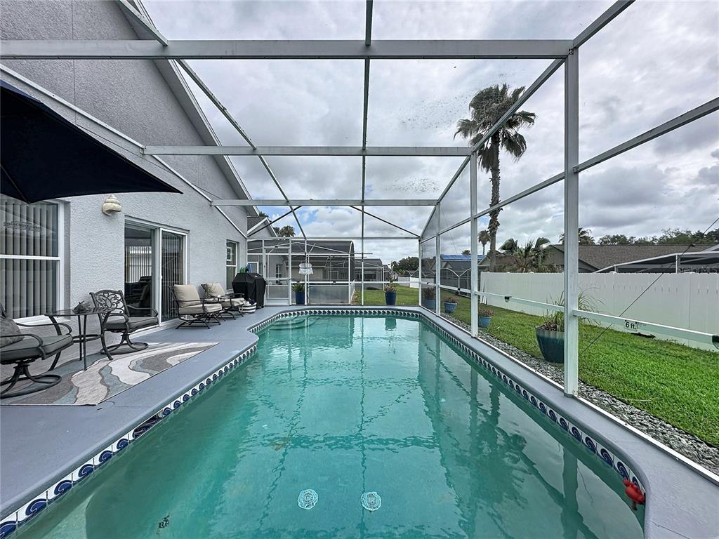 A screened-in swimming pool sits on a patio next to a house with outdoor furniture — 208 CASTLEMAIN CIRCLE, DAVENPORT, FL