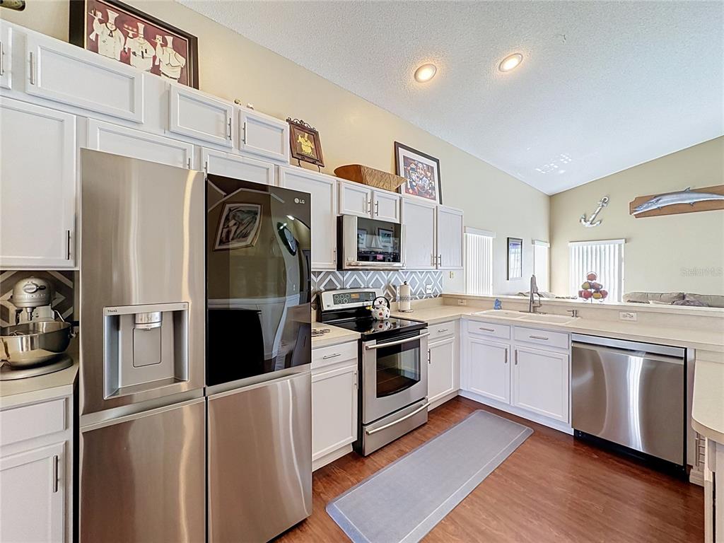 A kitchen features white cabinets, stainless steel appliances, and wood-look flooring — 208 CASTLEMAIN CIRCLE, DAVENPORT, FL