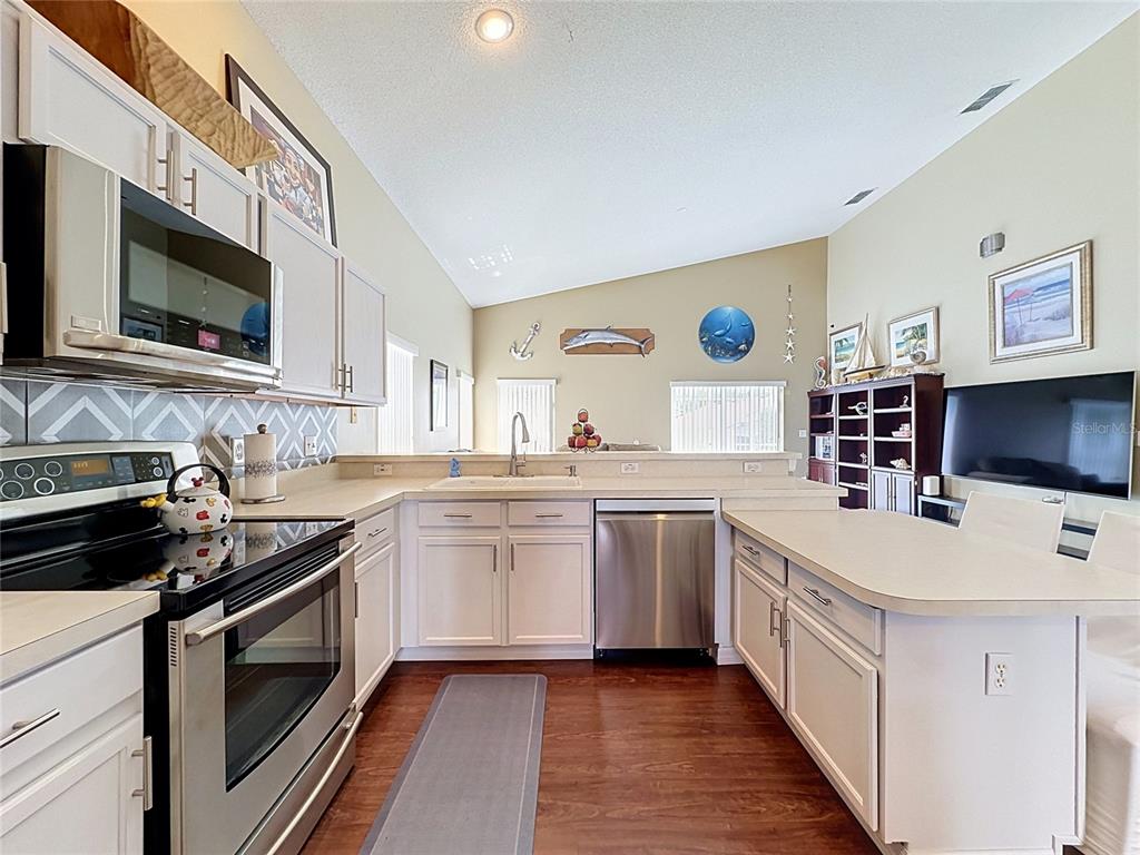 A kitchen features white cabinets, stainless steel appliances, a breakfast bar, and wood-look flooring — 208 CASTLEMAIN CIRCLE, DAVENPORT, FL