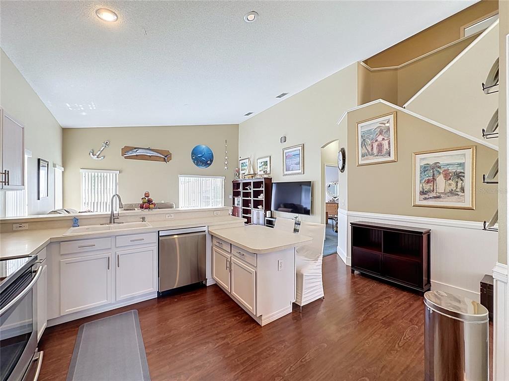 A kitchen with white cabinets, stainless steel appliances, and wood flooring opens to a living area — 208 CASTLEMAIN CIRCLE, DAVENPORT, FL
