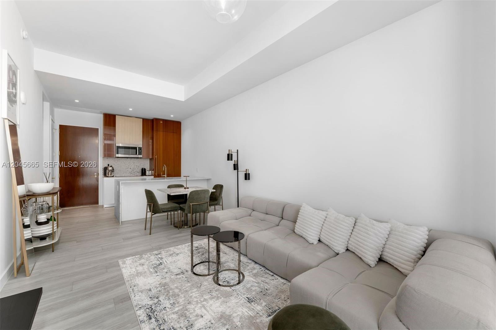 A modern living room features a grey sectional sofa, a small dining area, and kitchen cabinetry — 2655 S Bayshore Dr # 908, Miami FL 33133, MIAMI, FL