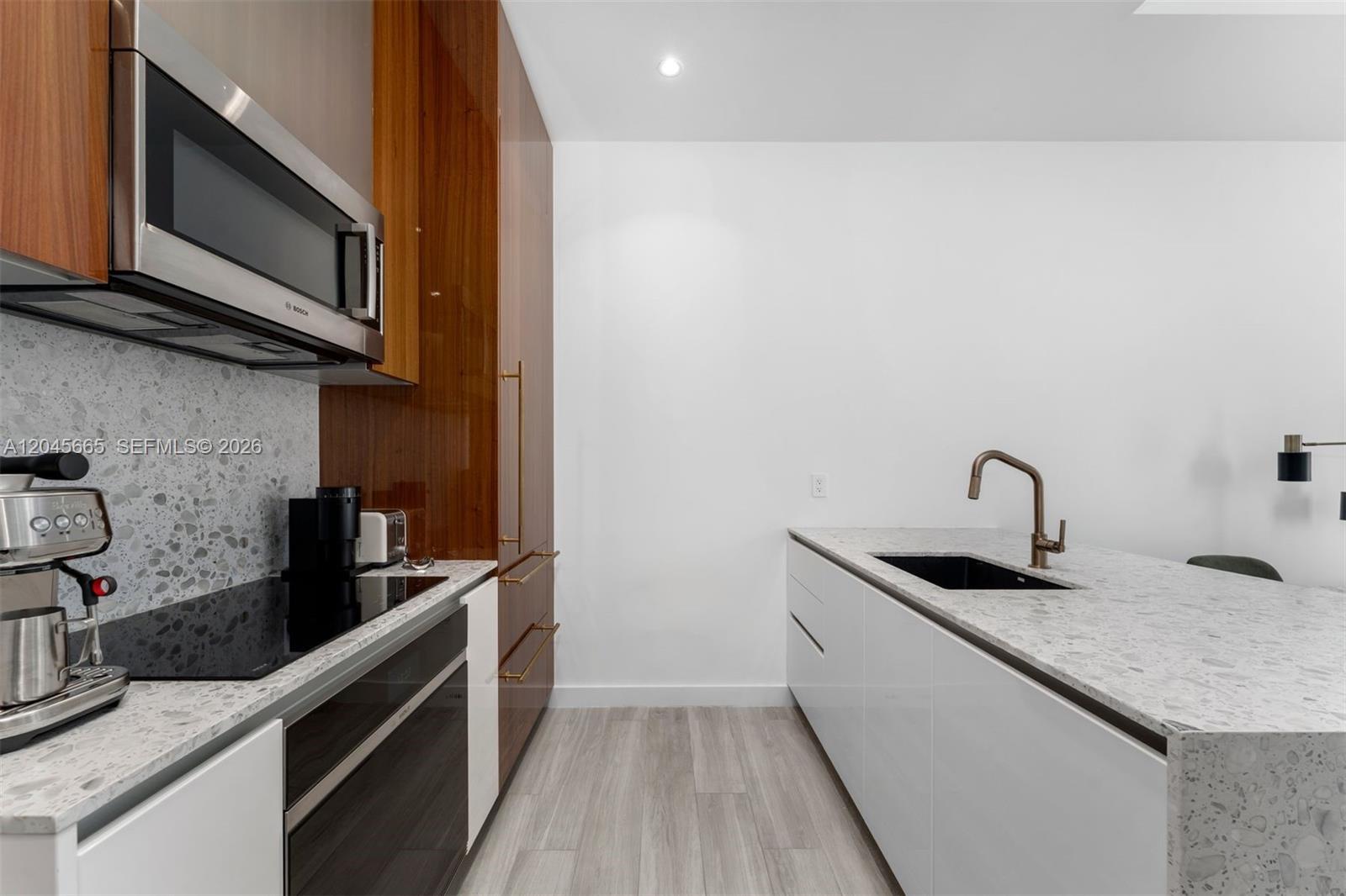 A modern kitchen features white cabinetry, wood-paneled storage, stone countertops, and stainless steel appliances — 2655 S Bayshore Dr # 908, Miami FL 33133, MIAMI, FL