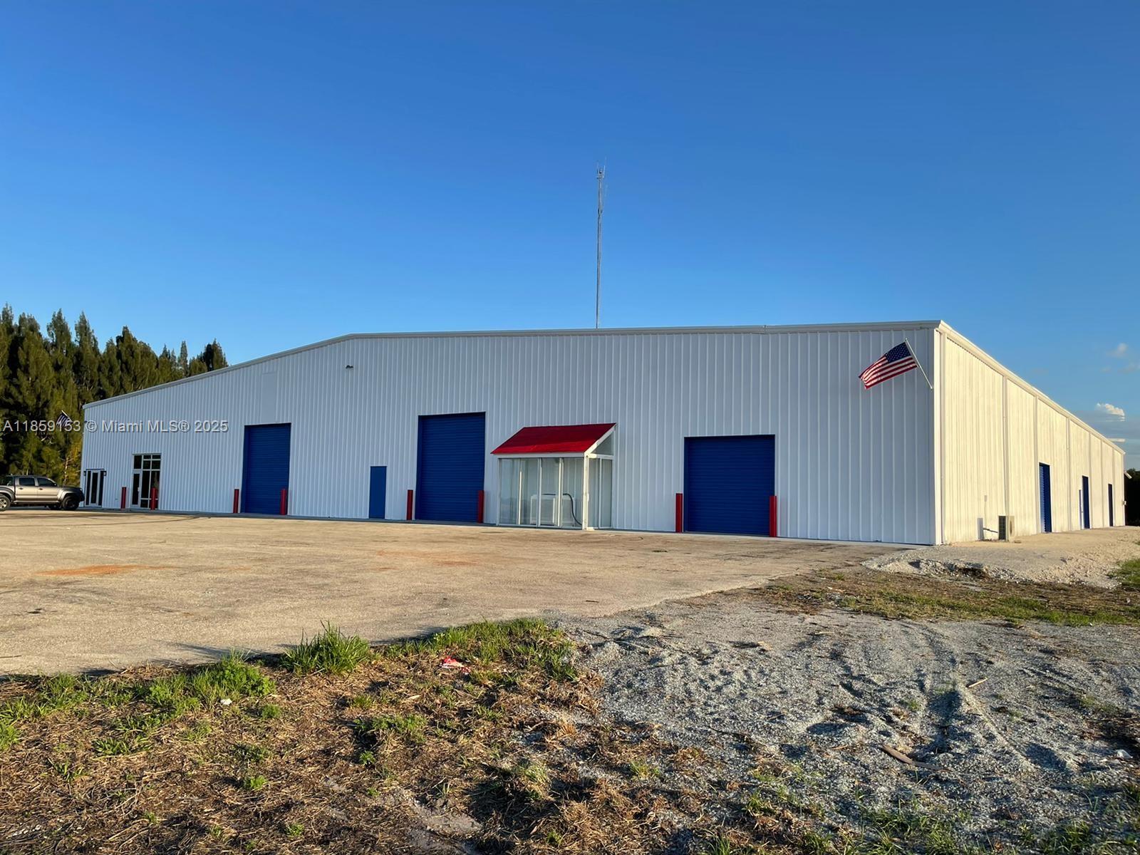 A white metal industrial warehouse building features blue roll-up doors and a red-canopied entrance — 14961 SR W78, Moore Haven FL 33471, MOORE HAVEN, FL
